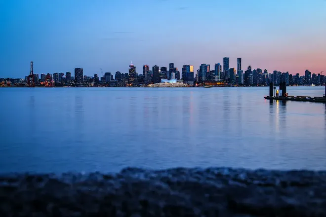 Die Silhouette einer Stadt jenseits des Wassers unter tiefblauem Himmel mit einem letzten rosa Leuchten.